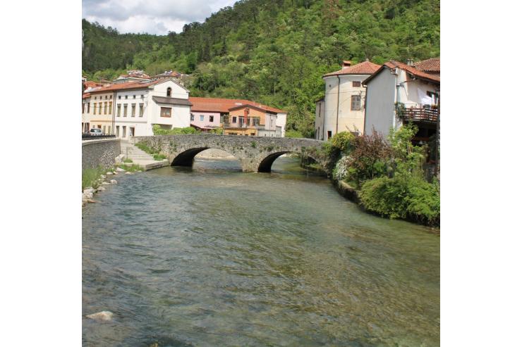 Fotografija prikazuje reko, ki teče pod mostom. V ozadju so hiše.